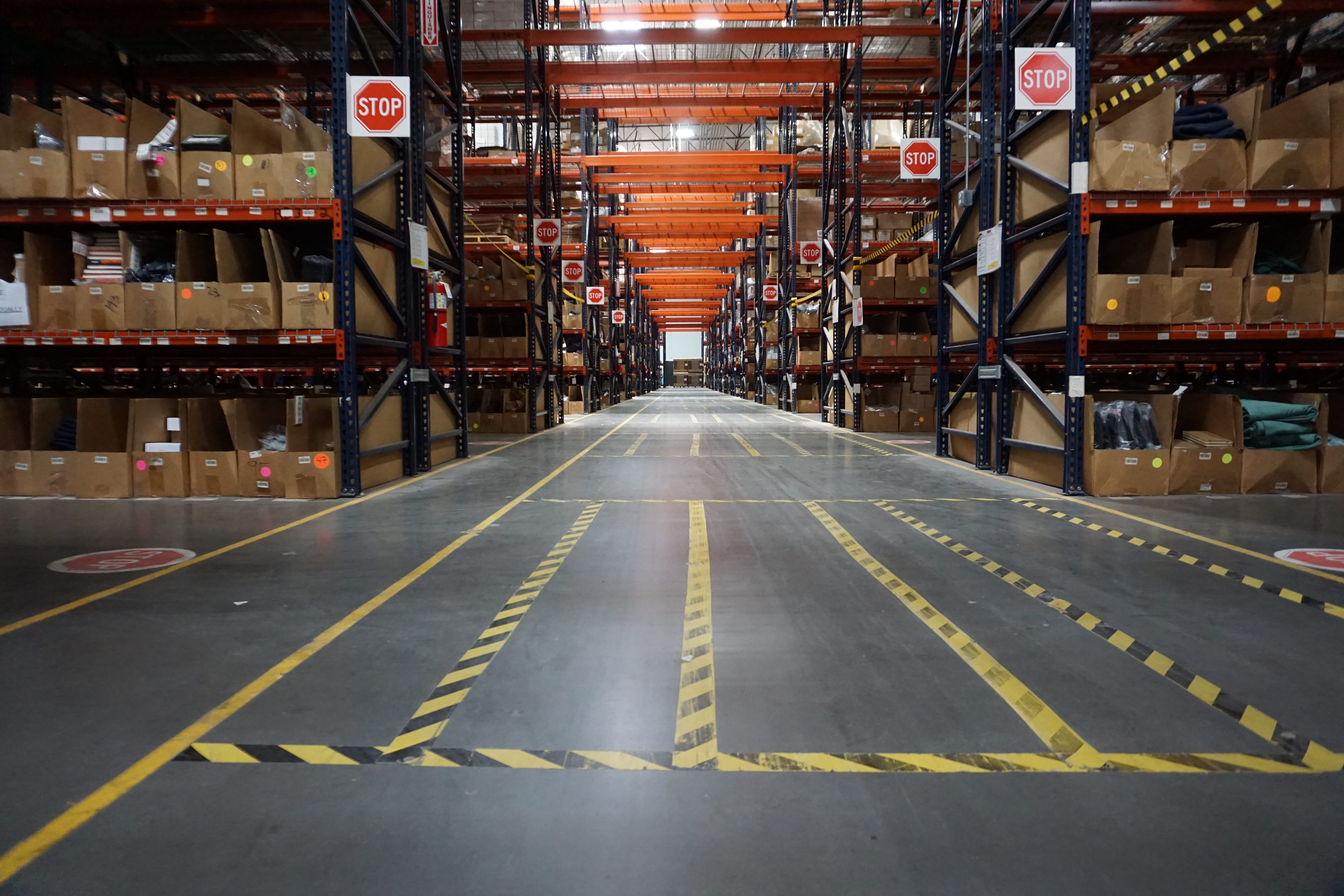 Warehouse aisle with tall shelves filled with boxes and multiple stop signs visible on racks and floor.