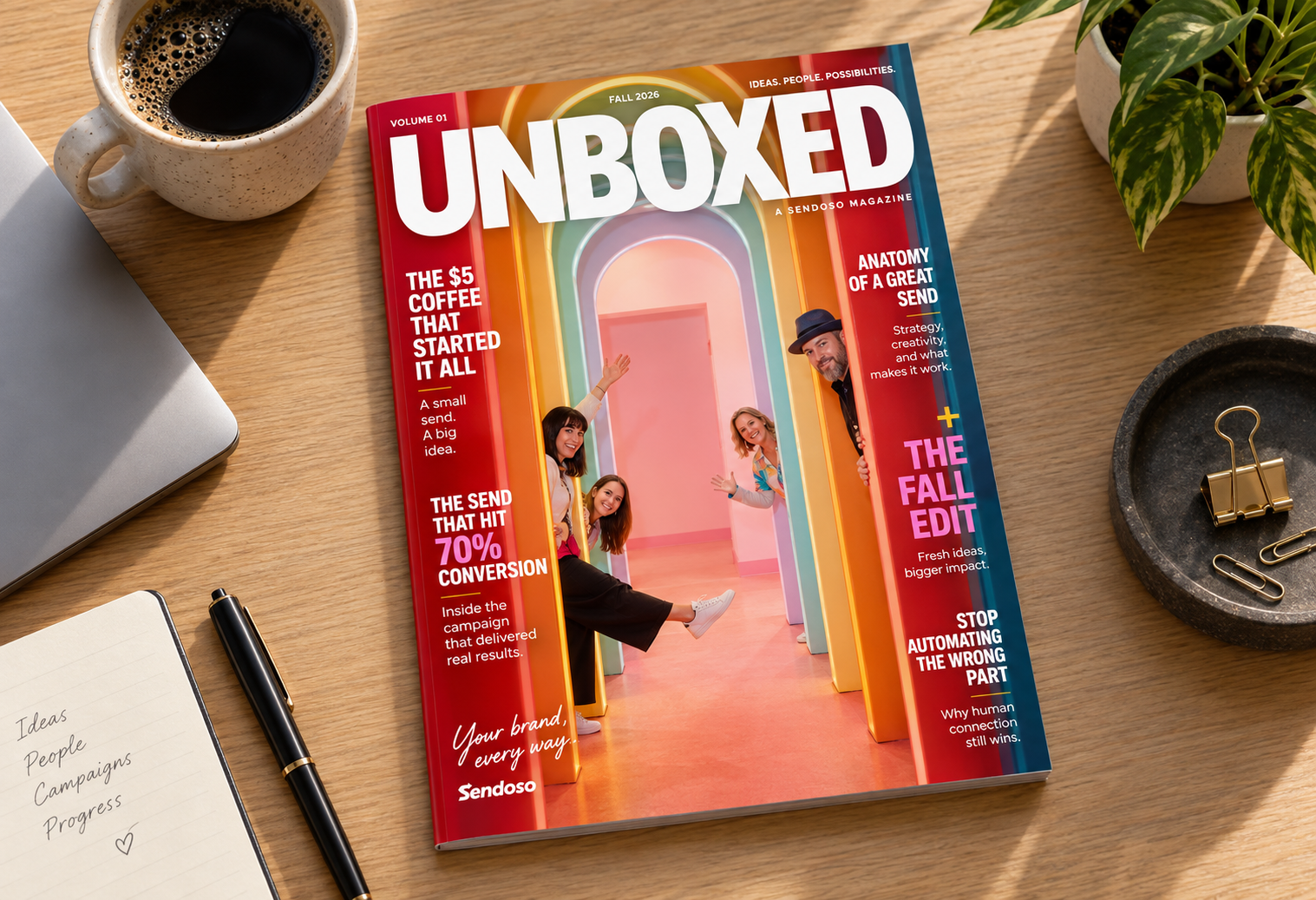 Fall 2026 volume 01 issue of Unboxed, a Sendoso magazine, on a wooden desk next to a cup of coffee, a notebook with handwritten words 'Ideas People Campaigns Progress' and a pen, and a small plant. The cover shows four people peeking and waving from colorful archways. Headlines include '$5 coffee that started it all,' '70% conversion send,' 'Anatomy of a great send,' 'The fall edit,' and 'Stop automating the wrong part.'