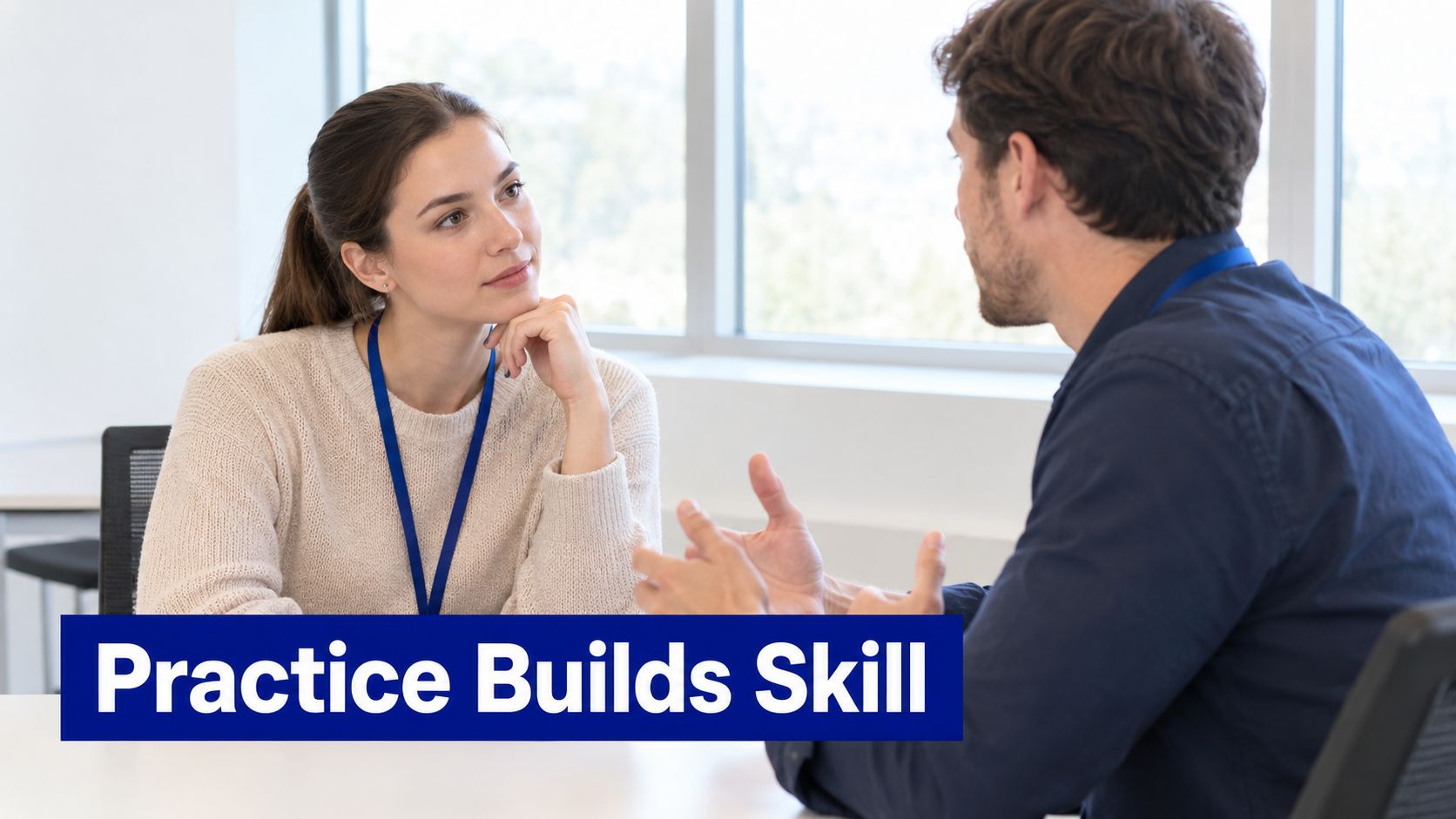 A professional woman and a man sitting at a desk engaged in a work conversation.