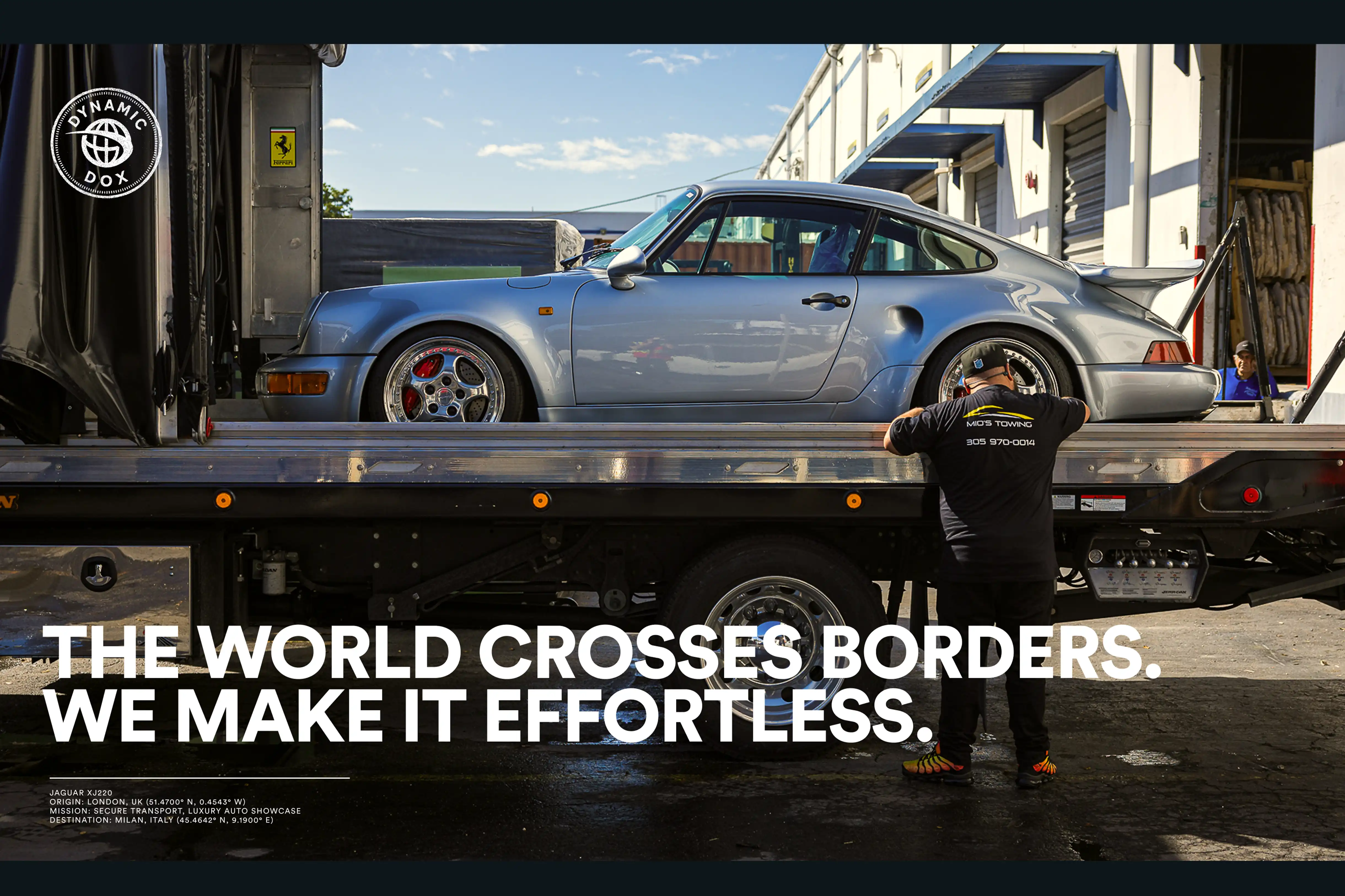 Silver classic sports car on a flatbed tow truck with a man wearing a Mios Towing shirt standing nearby.