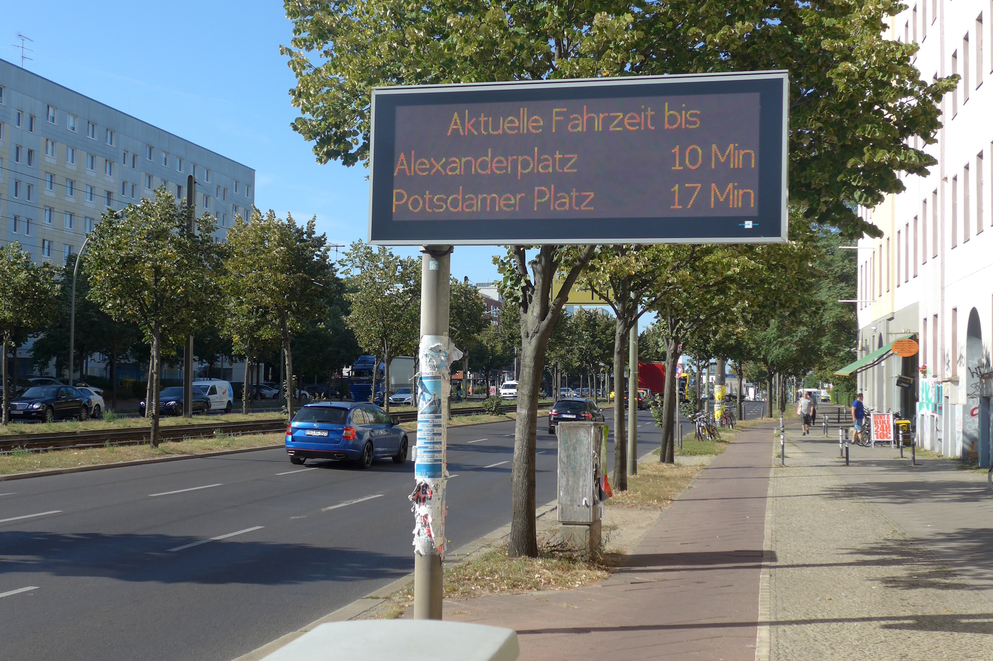 Digitale Anzeigetafel am Straßenrand einer Berliner Straße, Anzeige zeigt Fahrtweg bis zum Alexanderplatz Berlin sowie zum Potsdamerplatz an.