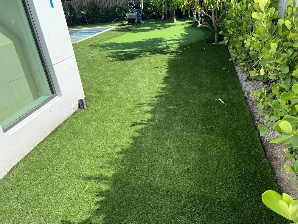 a backyard with artificial grass and a pool in the background
