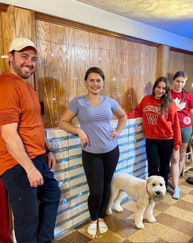Nick and Anastasia with family, their dog and a wall of boxes