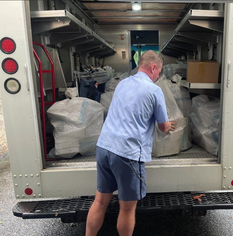 A mail carrier loading sacks of boxes into a USPS truck