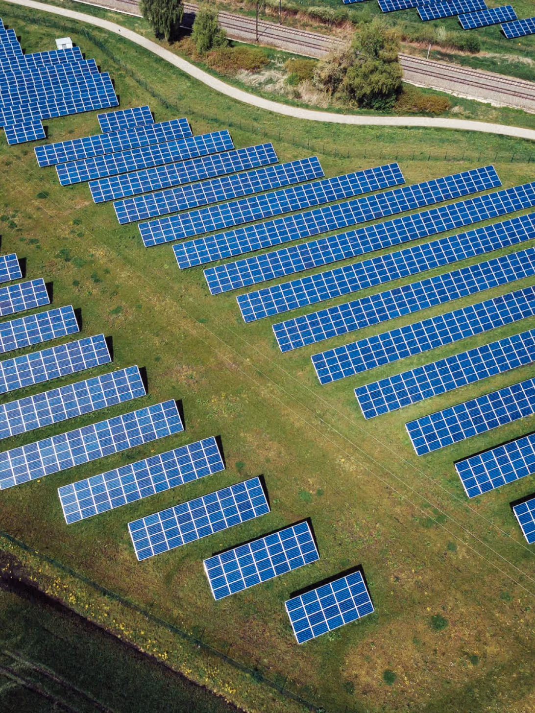 Aerial view of a large solar farm with evenly spaced rows of blue solar panels installed on a grassy field.