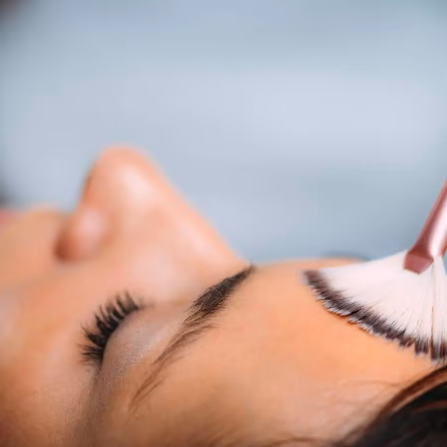 Nærbilde av en kvinne som får behandling, viser et lukket øye og en børste som påfører produkt tvers over pannen.