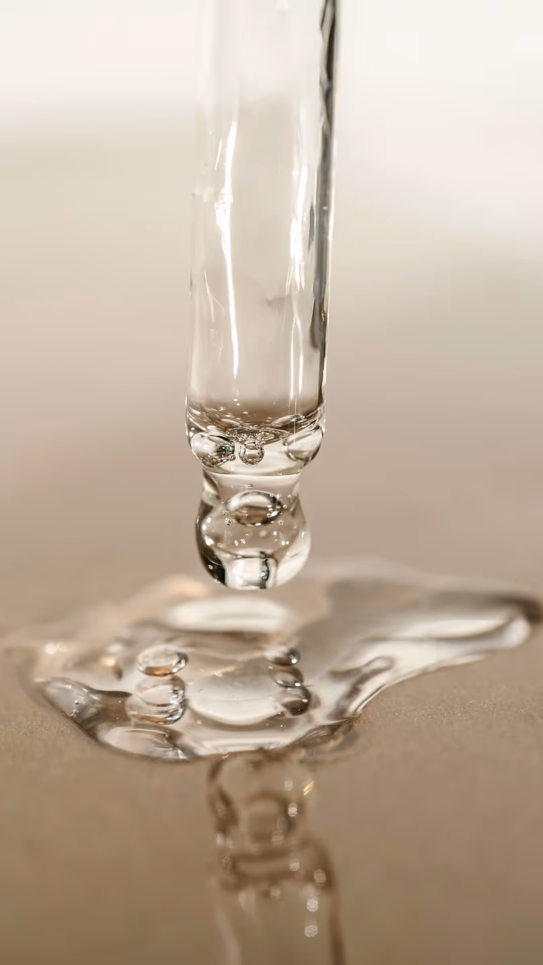 En vannstrøm fanget midt i strømmen og danner et sprut når den treffer en overflate. Scenen er satt mot en nøytral, uskarp bakgrunn, som fremhever klarheten til vannet og den flytende bevegelsen til spruten.