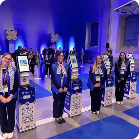Four women standing next to self-service kiosks in a modern event space with blue lighting.