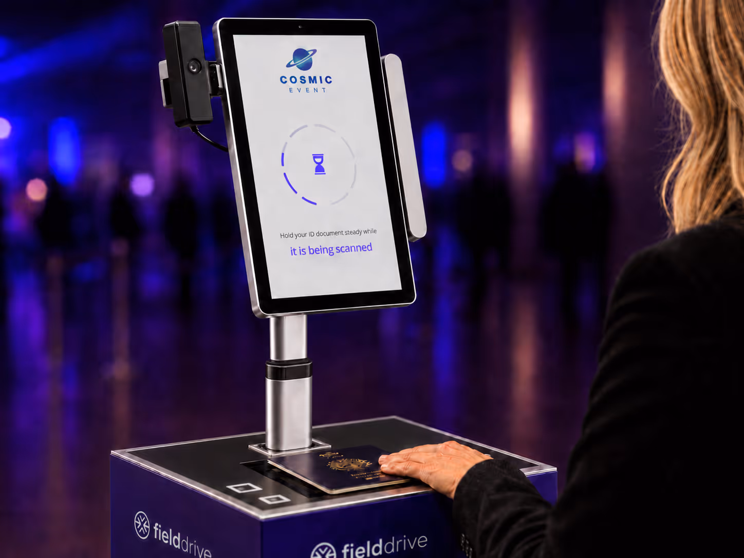 Person using a Fielddrive scanner to scan a passport with a screen showing a scanning message.