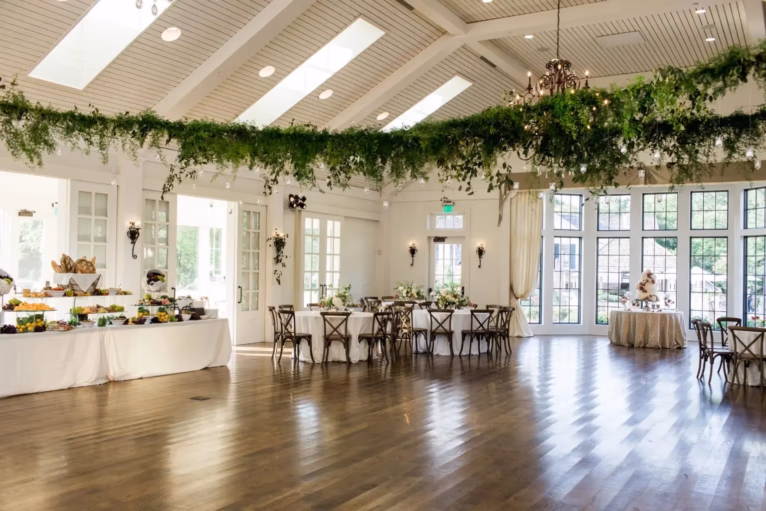 Ballroom reception featuring a banquet table, chandeliers, and greenery hung from the rafters.