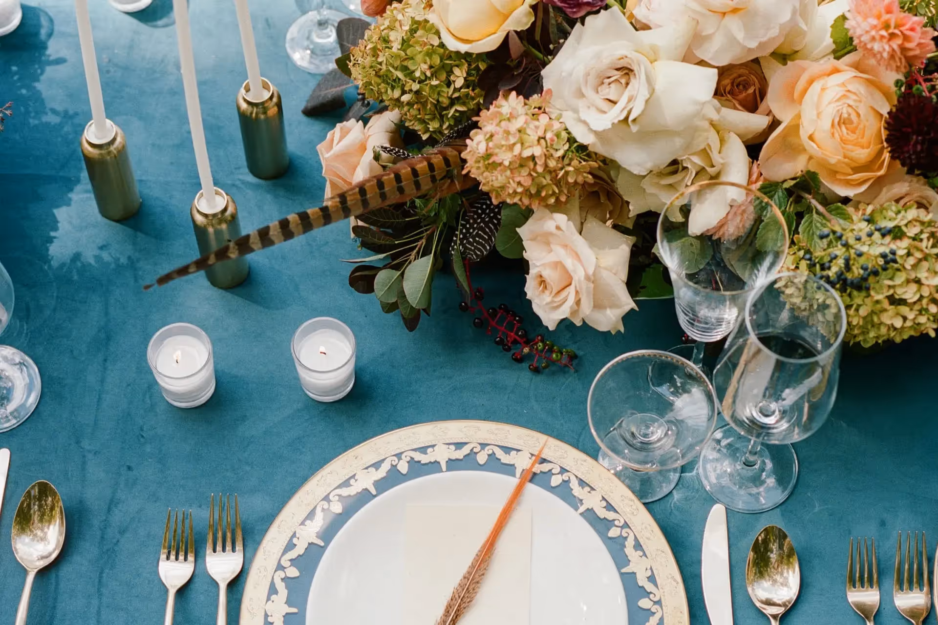 Close up of a wedding reception table decorated with custom dinnerware, votive candles, and beautiful floral centerpiece.