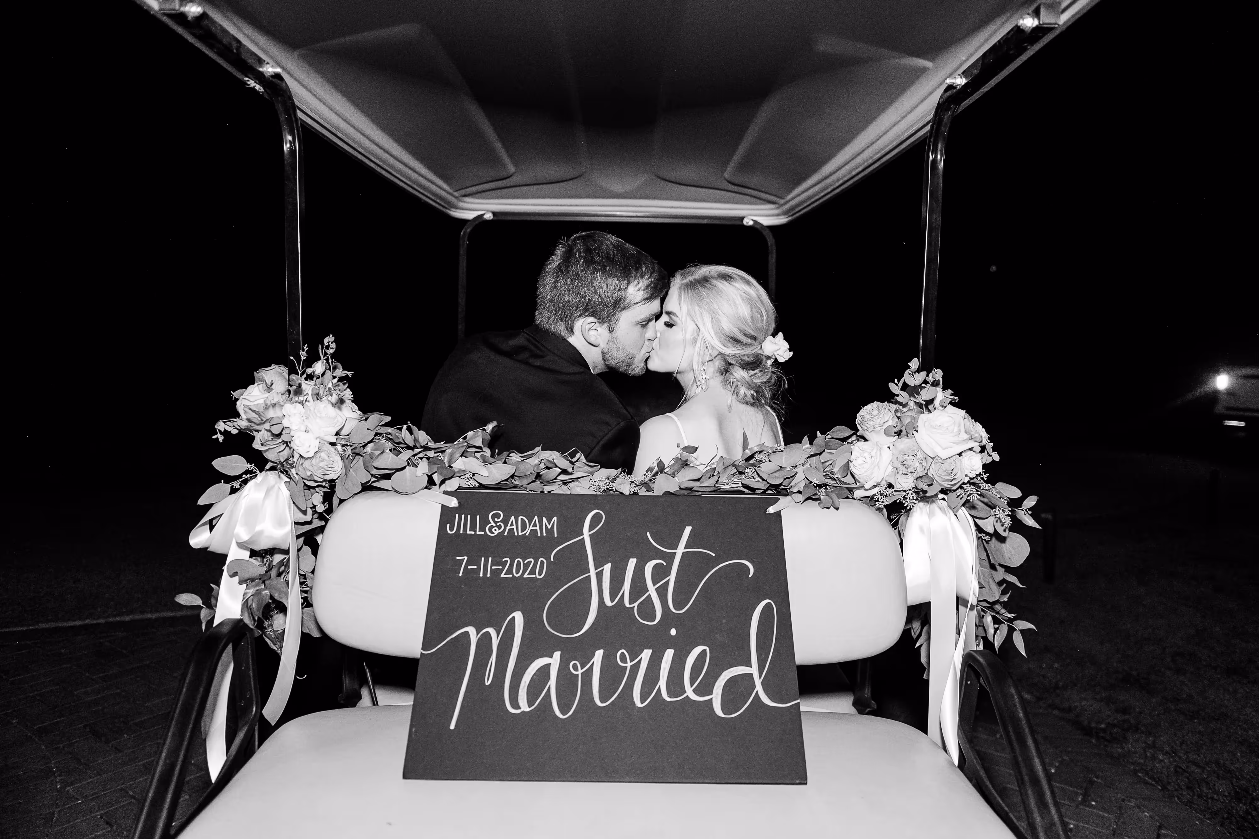 Newlywed couple shares a kiss in a golf cart adorned with "just married" sign.