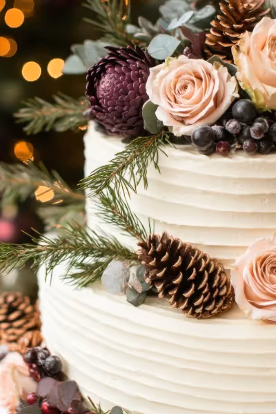 Forest themed rustic wedding cake with flowers, berries, and pine cone accents.