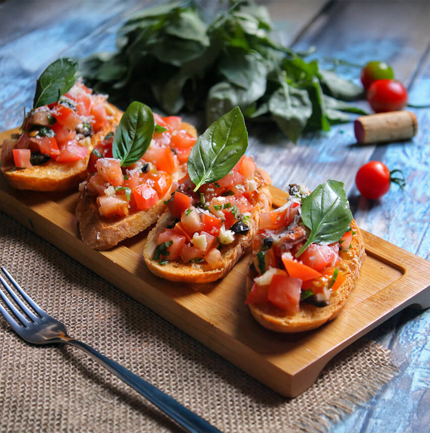 Charcuterie-style board featuring toasted bread topped with tomato and basil, accompanied by a fork and wine cork.