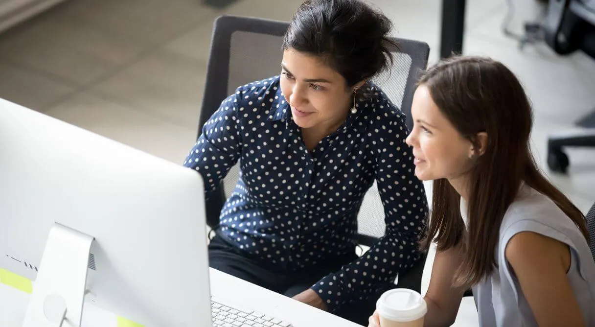two women sitting at a desk looking at a computer screen
