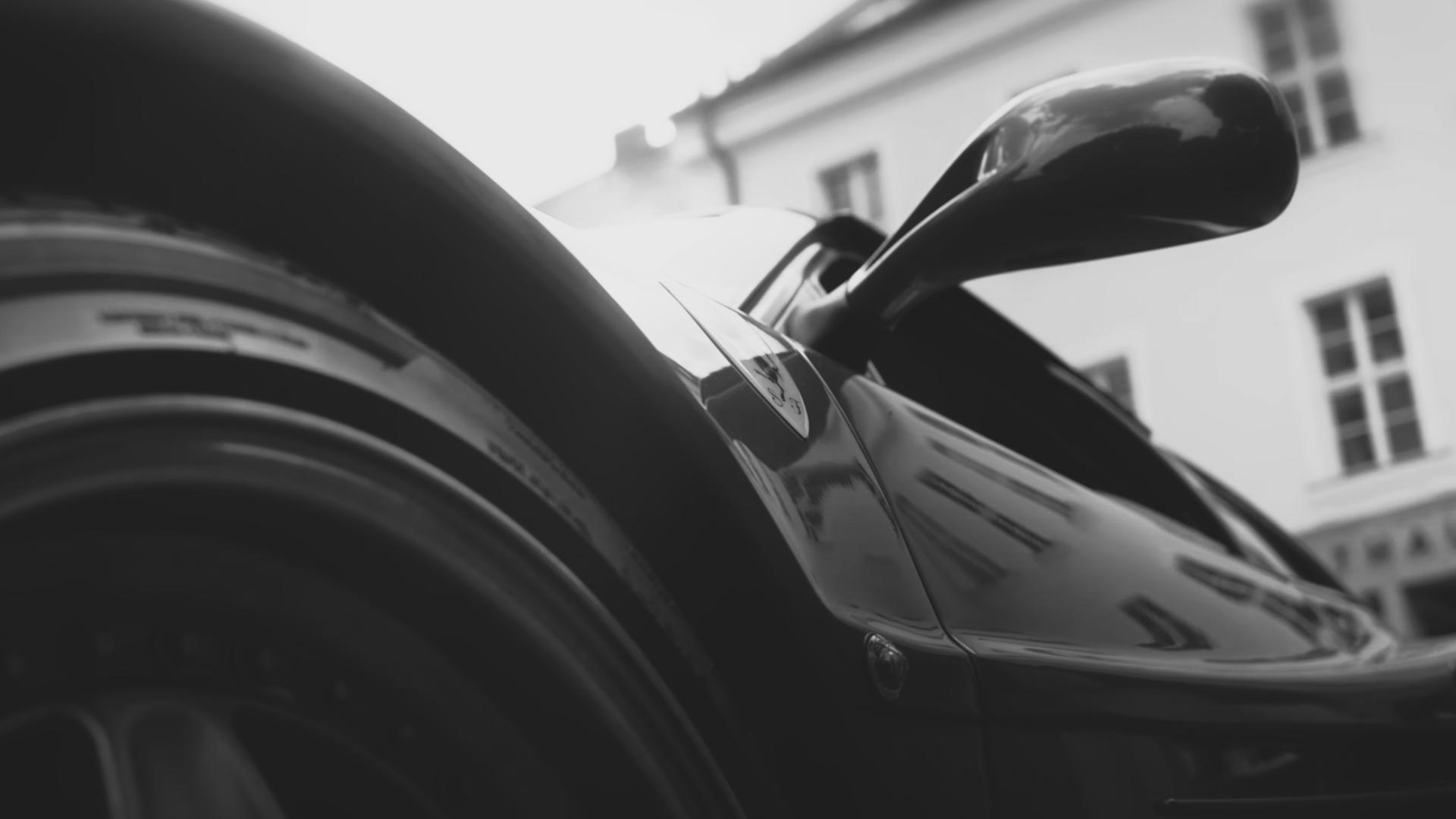 Close-up low-angle view of a black sports car's front wheel, side mirror, and side panel with reflections.