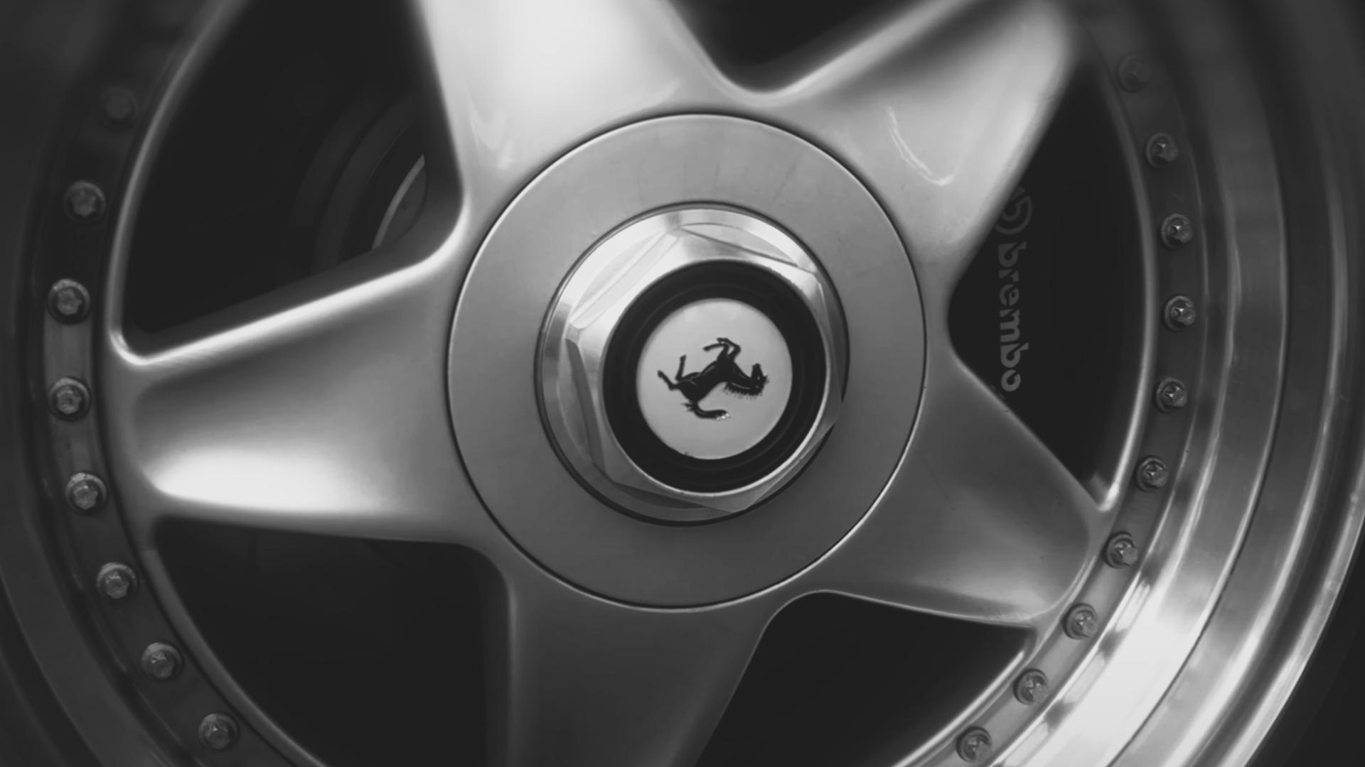 Close-up of a metallic car wheel rim with the Ferrari prancing horse emblem in the center and Brembo brake caliper visible behind.