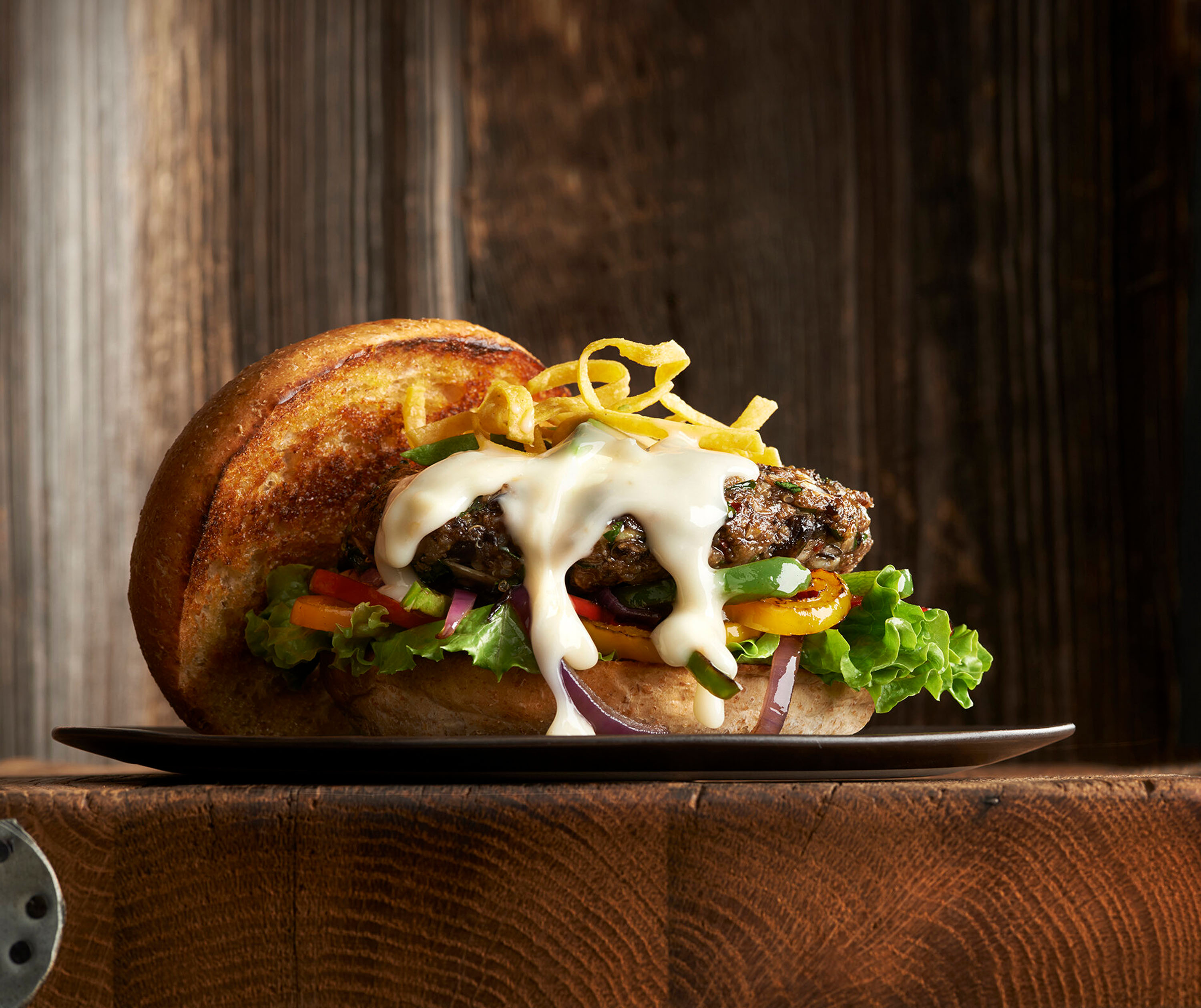 A Photograph of a thick hamburger on a wooden surfaces, covered in Chef-mate Cheese Sauce. Shot by Ralph Smith.
