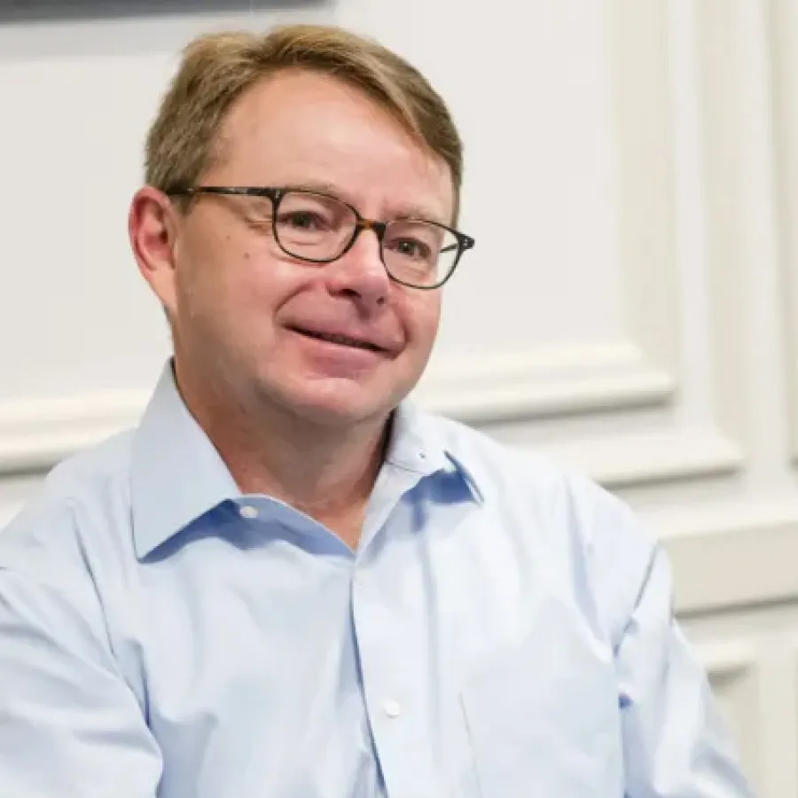 Middle-aged man with glasses wearing a light blue collared shirt smiling slightly in an indoor setting.