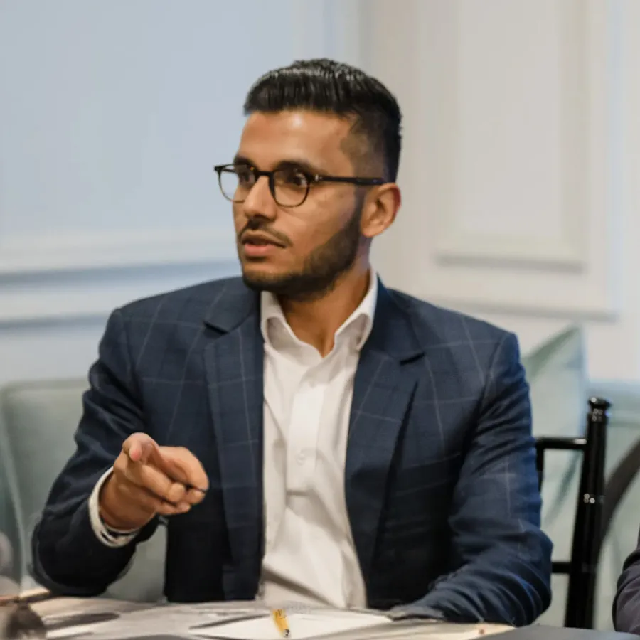 Man in glasses and suit jacket gesturing with his hand during a meeting.