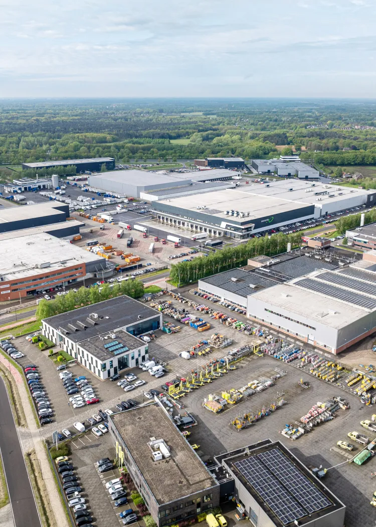 Aerial view of an industrial complex with warehouses, parking lots, and equipment storage surrounded by greenery.