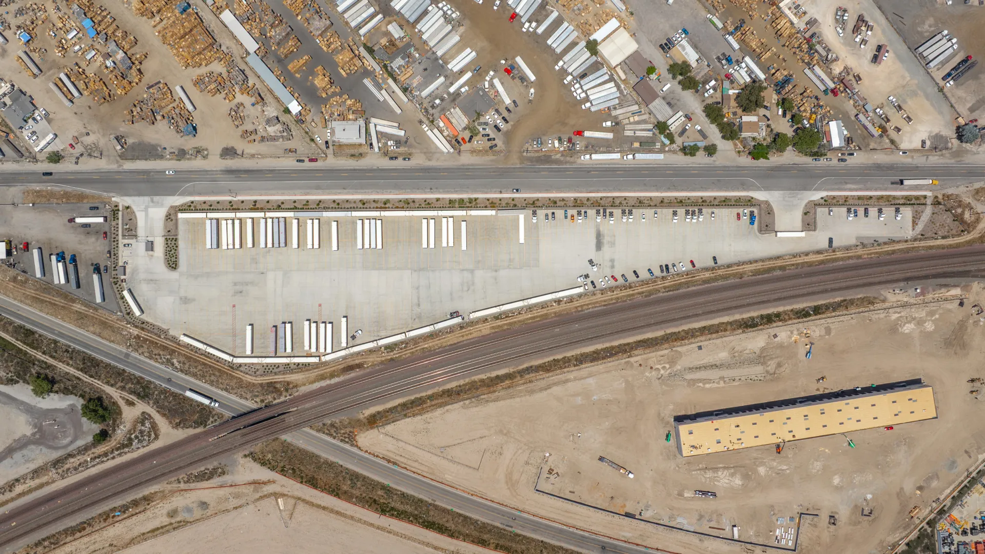 Aerial view of an industrial area with trucks, trailers, a large parking lot, and railway tracks crossing diagonally.