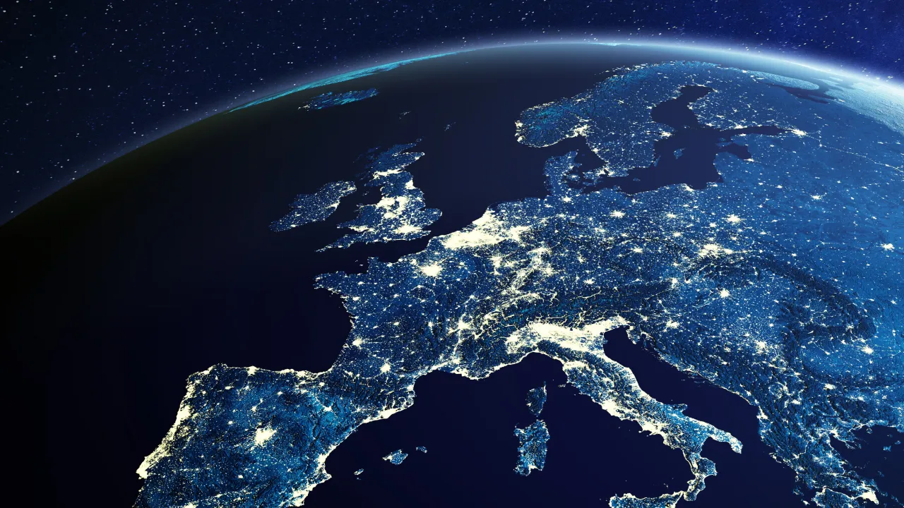 Satellite view of Europe at night showing city lights and the curvature of the Earth against stars.