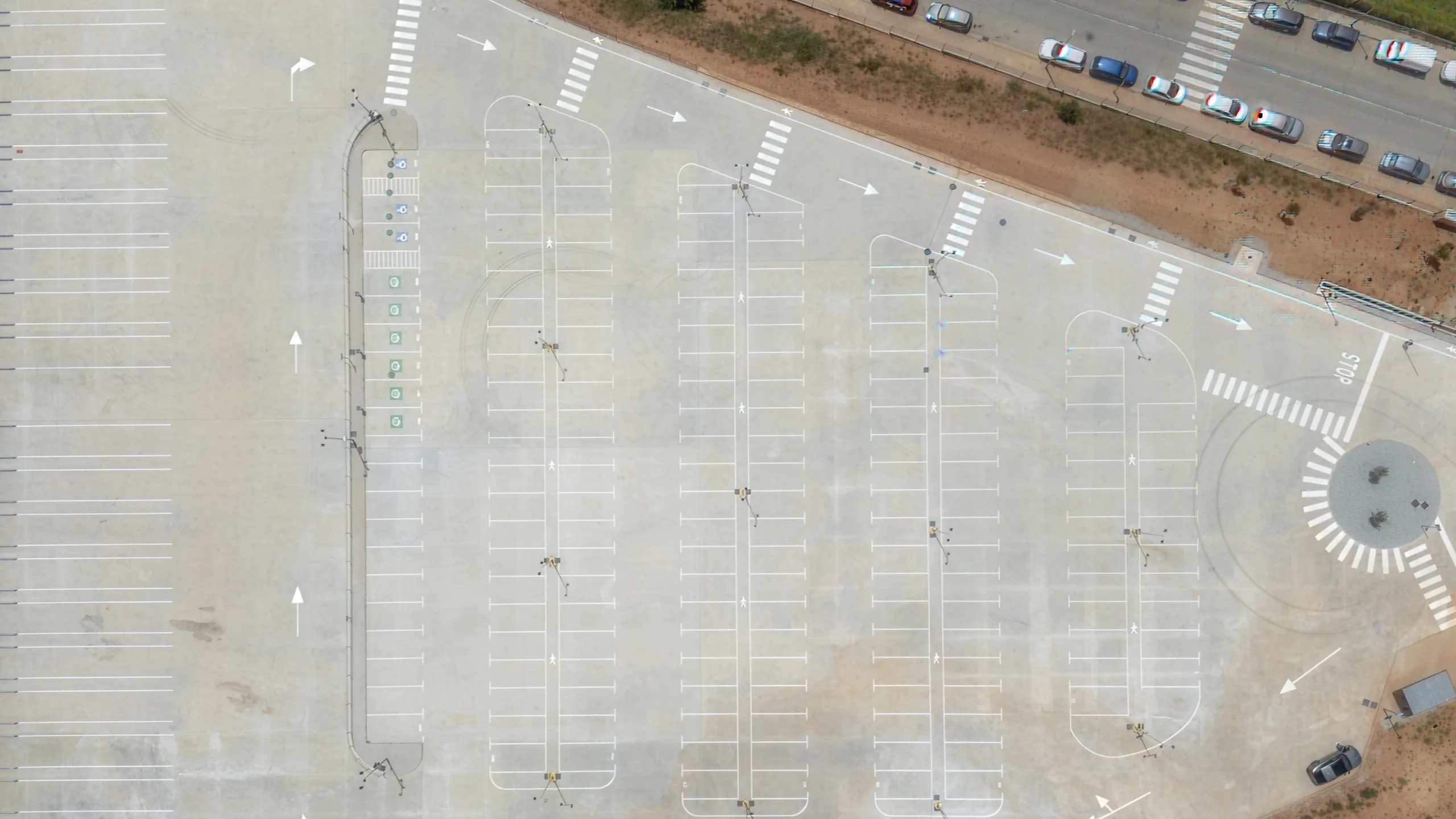 Aerial view of a large mostly empty parking lot with marked handicap spaces and adjacent road with parked cars.