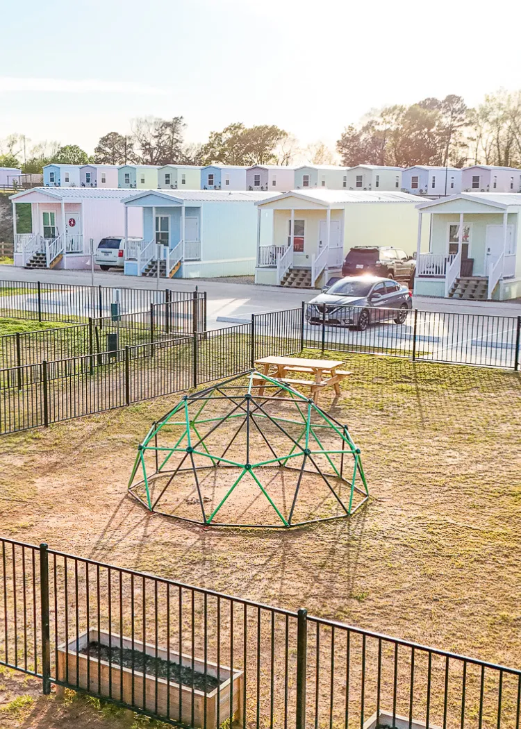 Small houses behind fenced yard with dome climber and picnic table in sunny outdoor area.