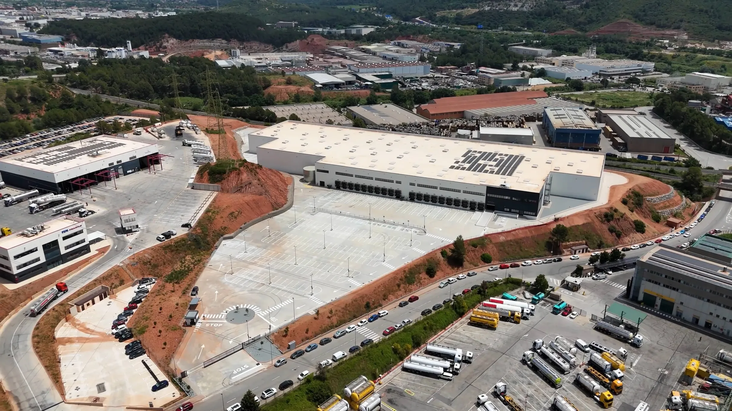 Aerial view of a logistics park with warehouse buildings, parking lots, trucks, and surrounding roads.