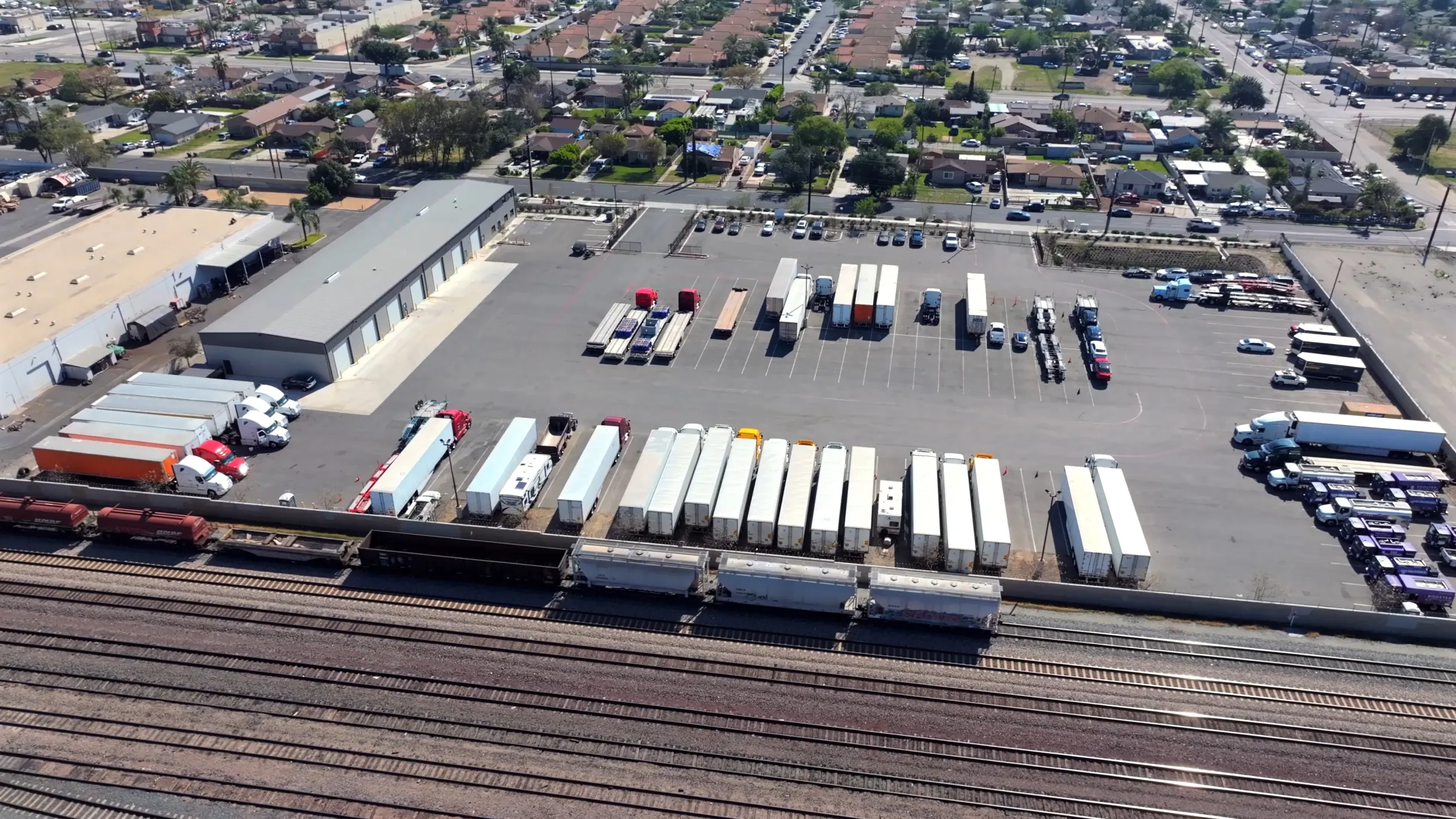 Aerial view of trucks, trailers, and railcars parked at a large freight yard near a residential area.