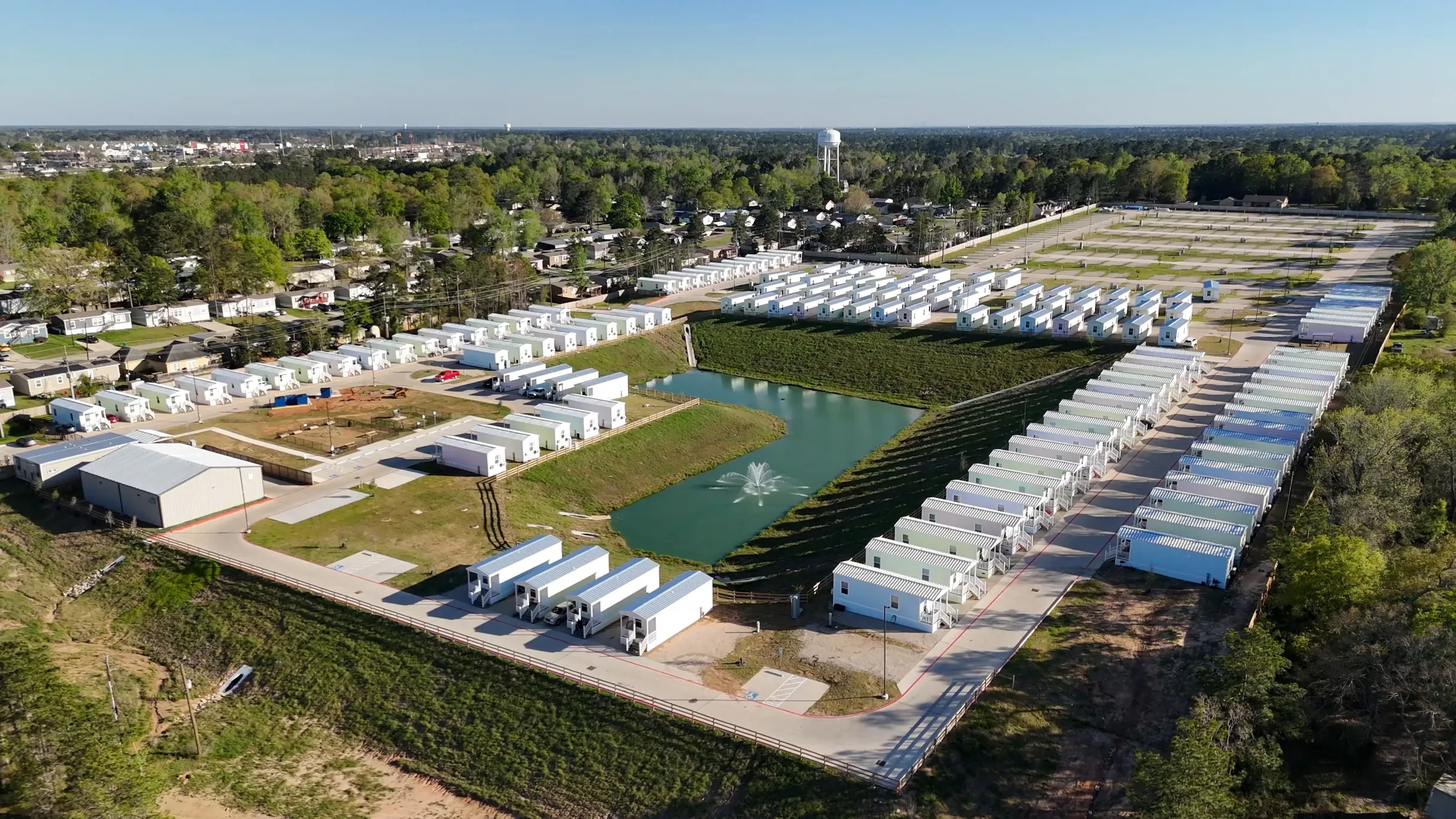 Aerial view of a small housing community with white modular homes around a pond with a fountain.
