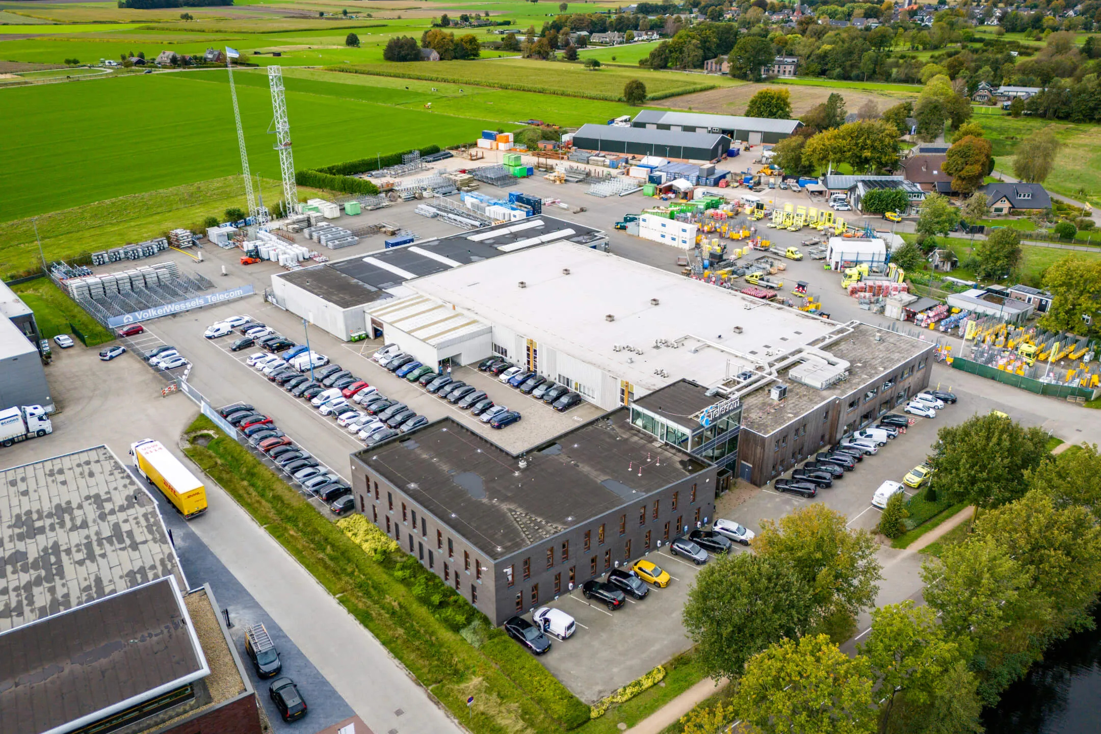 Aerial view of an industrial complex with parked vehicles, storage areas, and rural fields surrounding it.