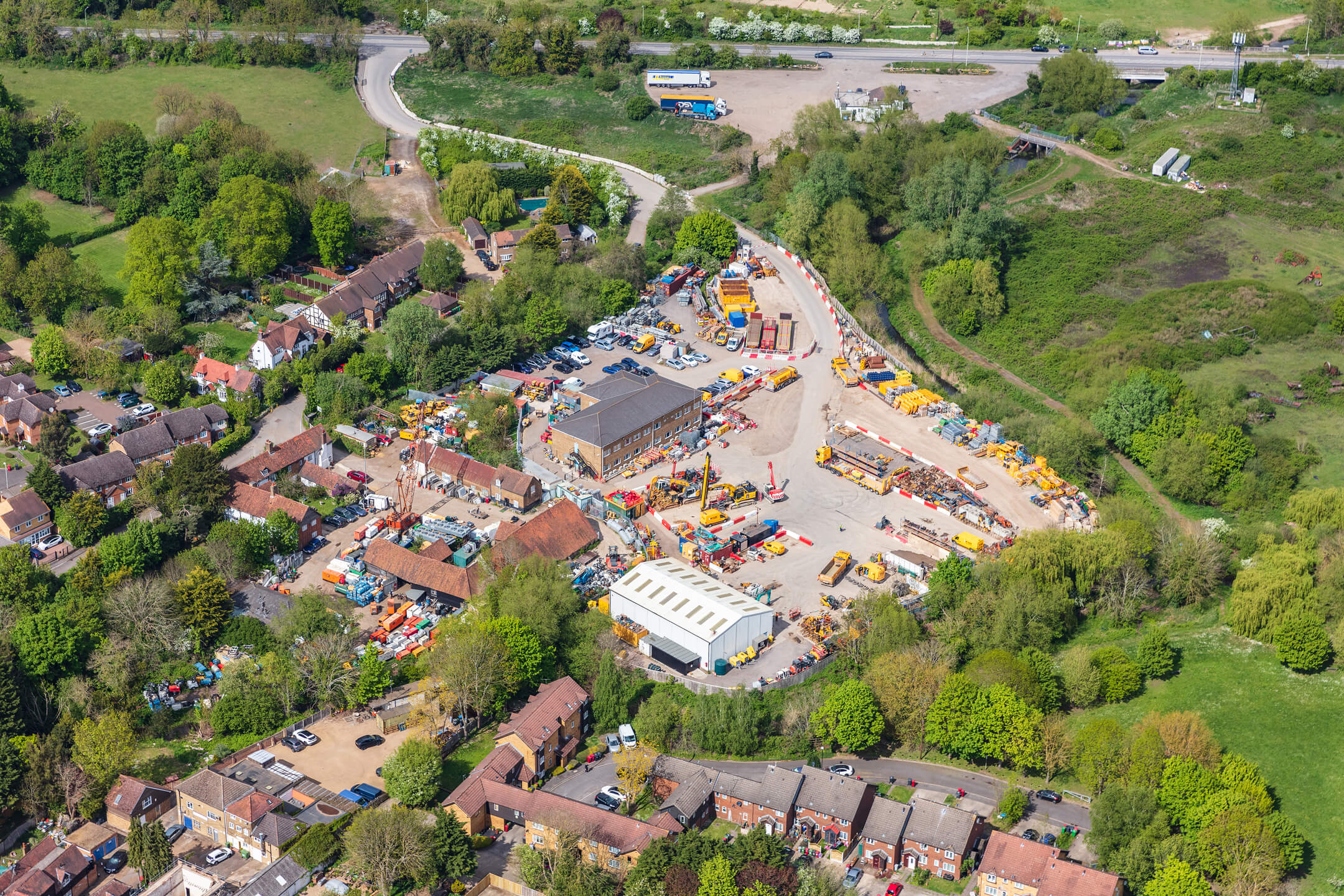 Aerial view of a construction equipment yard surrounded by houses and green trees.