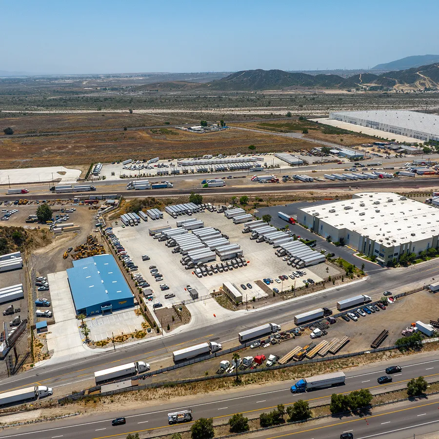Aerial view of a logistics hub with warehouses, parked trailers, trucks, and highways in a dry landscape.