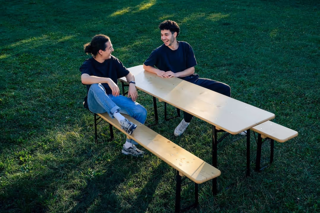 Bierbank-Flitzer Jonas und Valentin sehen sich auf einer Bierbank sitzend im Sonnenlicht an.