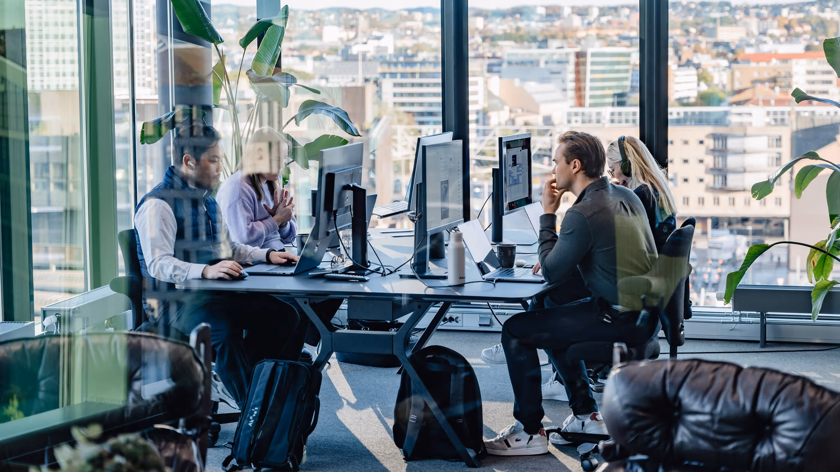 Fire personer sitter foran hver sin skjerm i et kontorlandskap