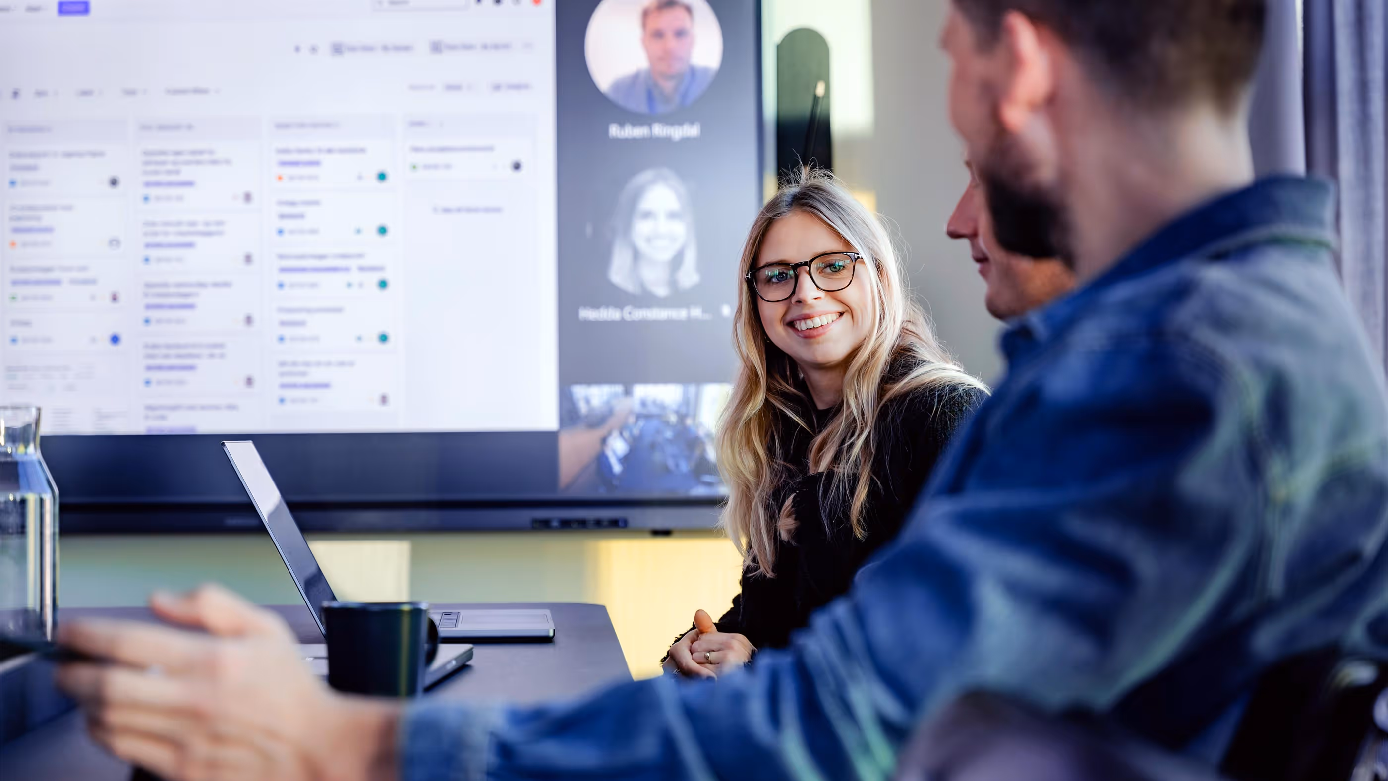 Smilende kvinne med teams på stoskjerm bak seg