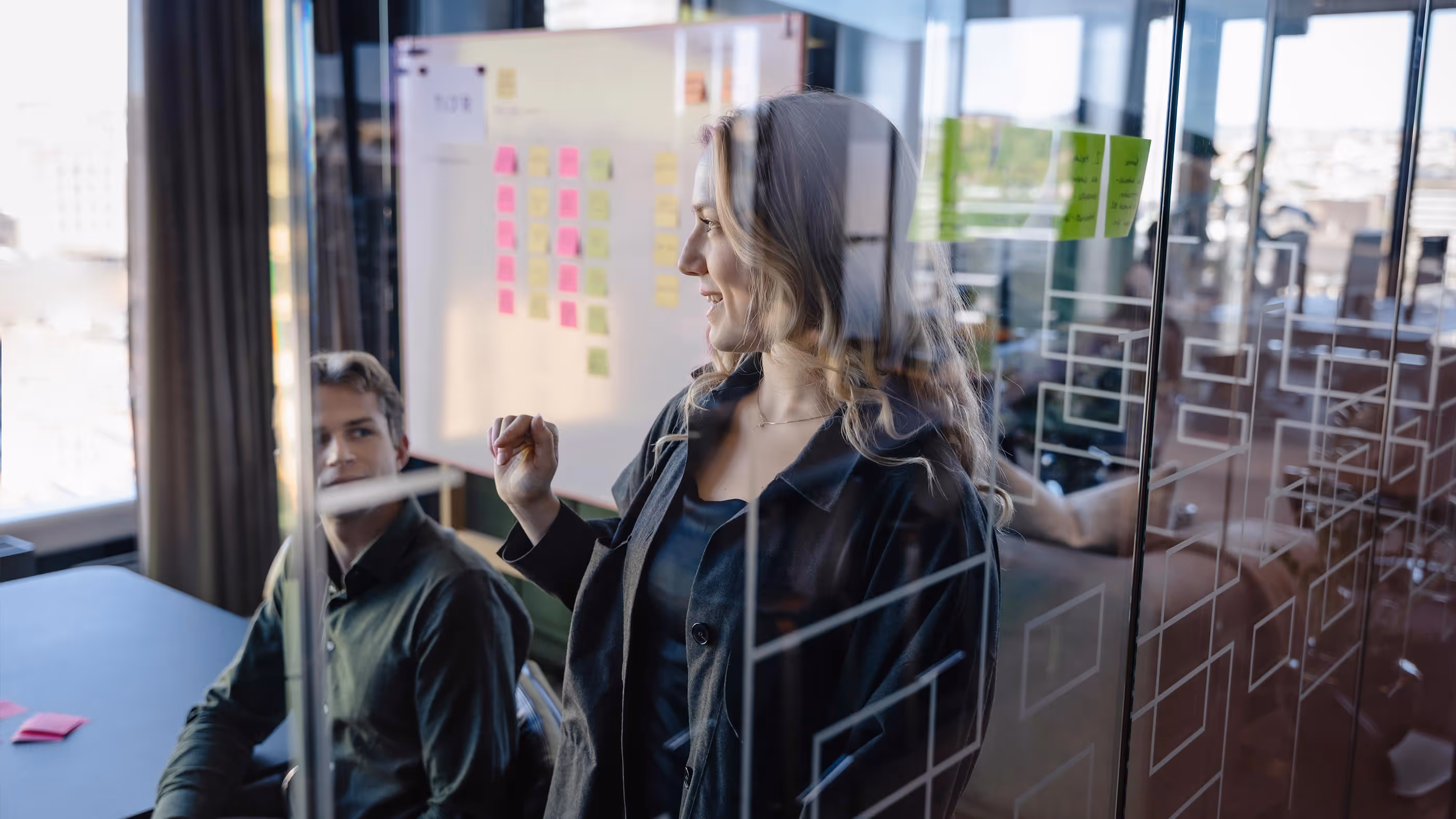 En kvinne og mann stårbak en glassvegg med post-it lapper