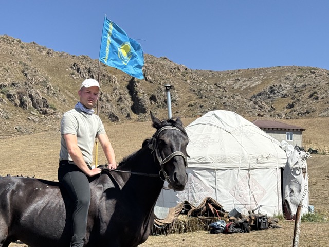 Rider in front of a yurt and the Kazakh flag at the summer pasture camp