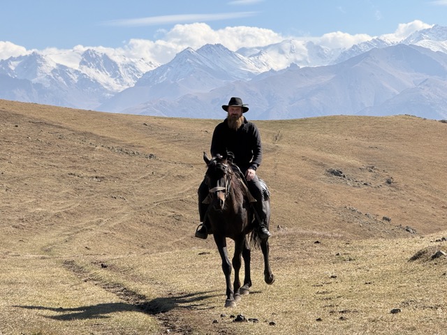 Guide in a hat on a black horse, with the snow-capped Tian Shan peaks behind