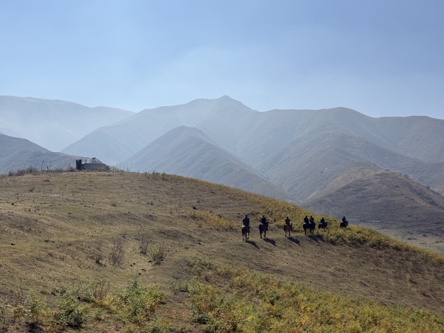 Line of riders on a hillside, a yurt in the misty distance