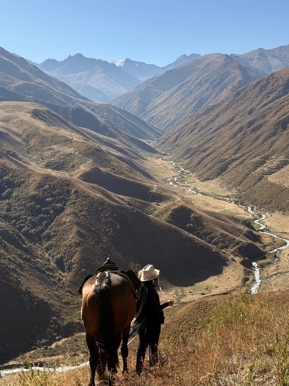 Rider leading her horse above a valley and its river in autumn