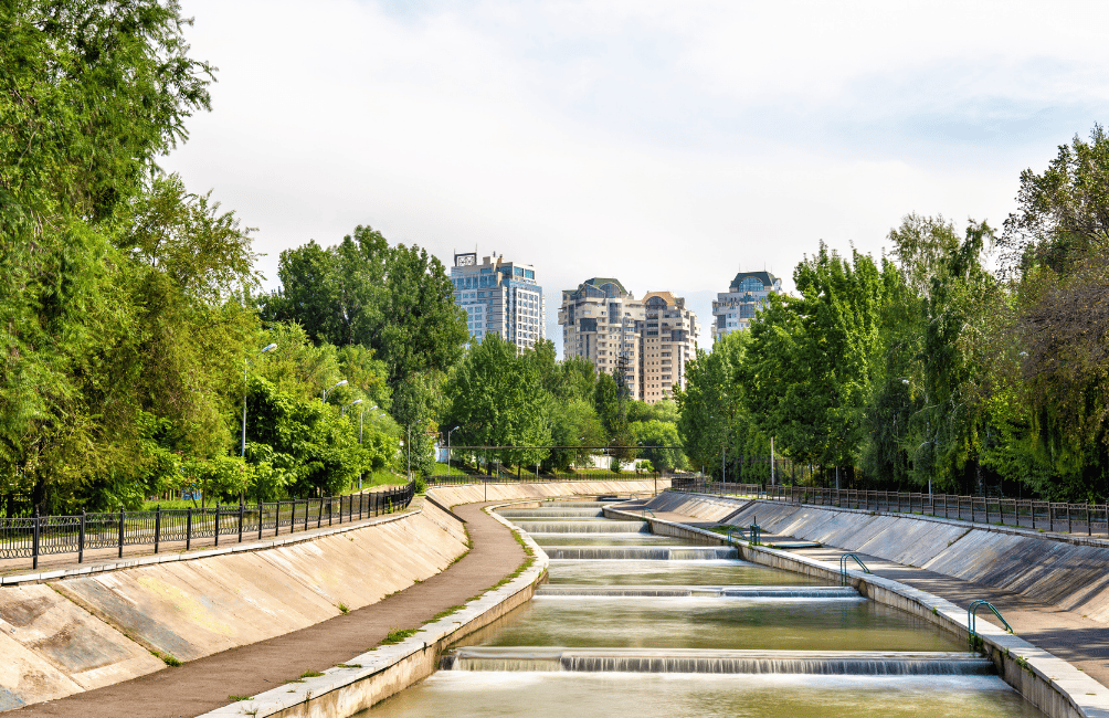 A tree-lined canal in the Esentai neighborhood of Almaty, with modern buildings in the background.