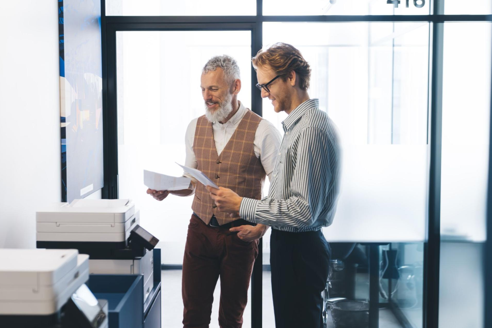 Two businessmen review pages at the printer.