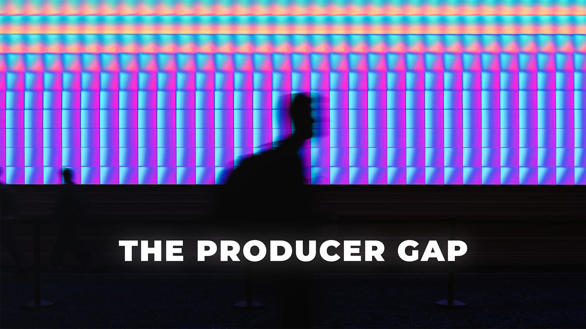 Silhouetted figure walking past a vibrant, high-resolution LED video wall at a corporate conference with the text 'THE PRODUCER GAP' centered in the foreground.