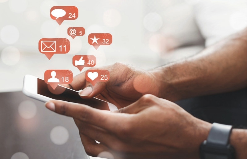 Person sidder med smartphone, hvor der kommer ikoner med hjerter, thumbs up og talebobler op fra