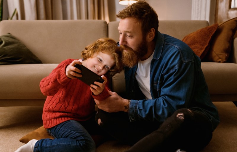 Forælder og barn sidder på gulvet og kigger på en smartphone