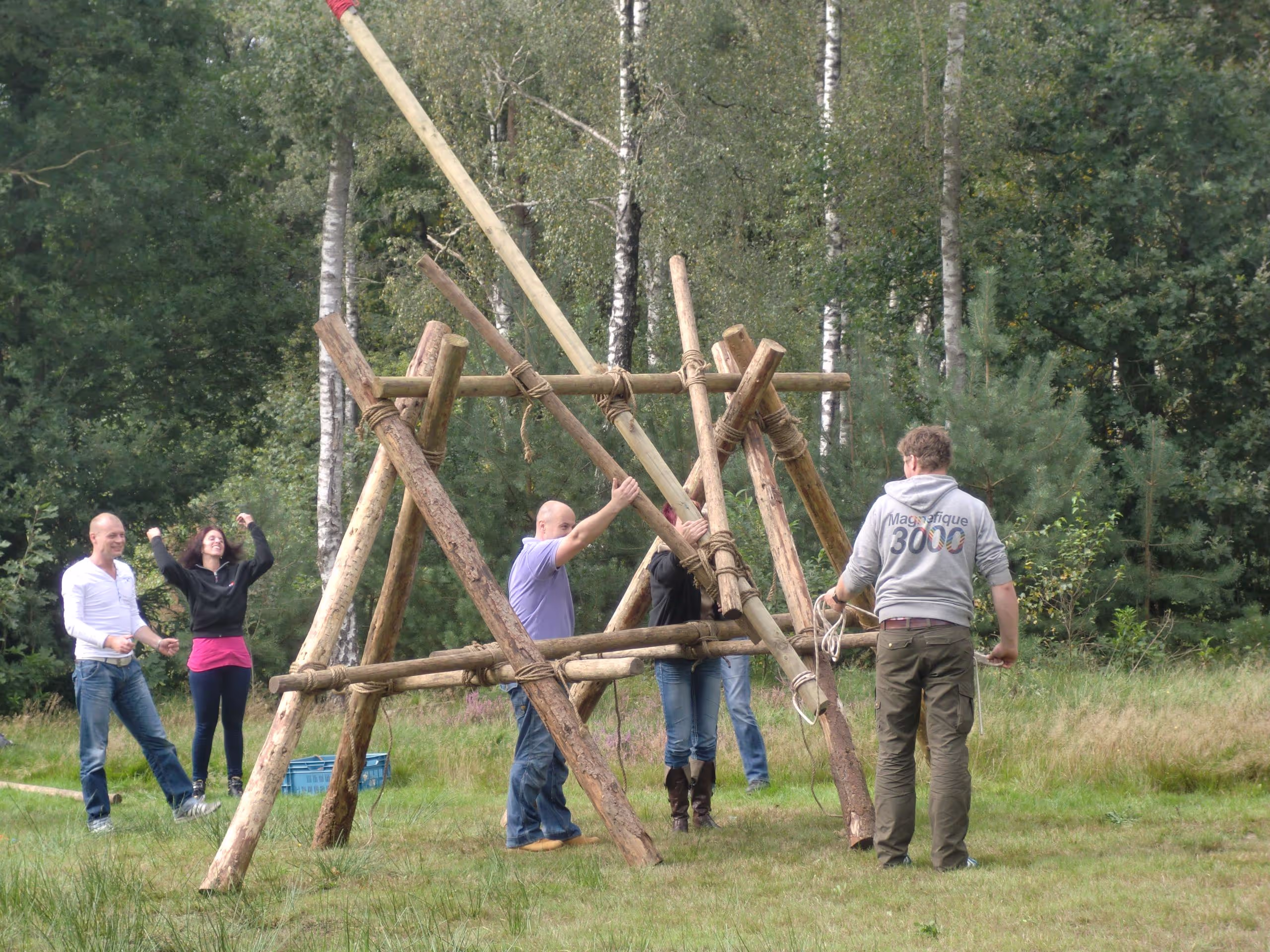 In een bosrijke omgeving wordt er met houten palen en touwen een katapult gemaakt