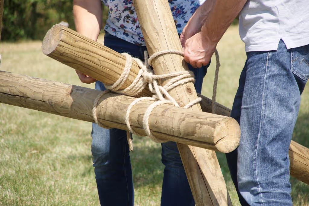 Drie houten palen zijn aan elkaar geknoopt met een wit touw